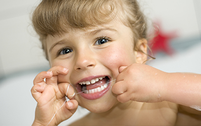 A young girl cleaning her teeth with dental floss