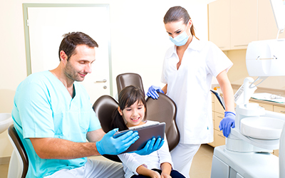 A child sittig in a dental chair with the dentist discussing with her. 