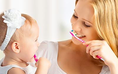 A young child and mother brushing their teeth together