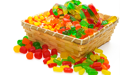 A basket full of chewy and sugary candy such as gummy worms and candy corn