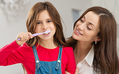 A girl brushing her teeth with her mom