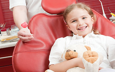 A young girl sitting in a dental chair holding a teddy bear
