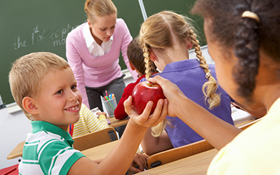 Children in classroom ahnding apple over to another child