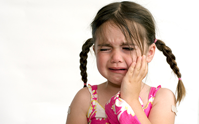 A young girl holding the side of her mouth in pain
