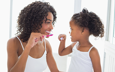 A mother and young girl brushing their teeth together