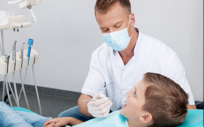 Young boy sitting in dental chair while dentist looks at his teeth